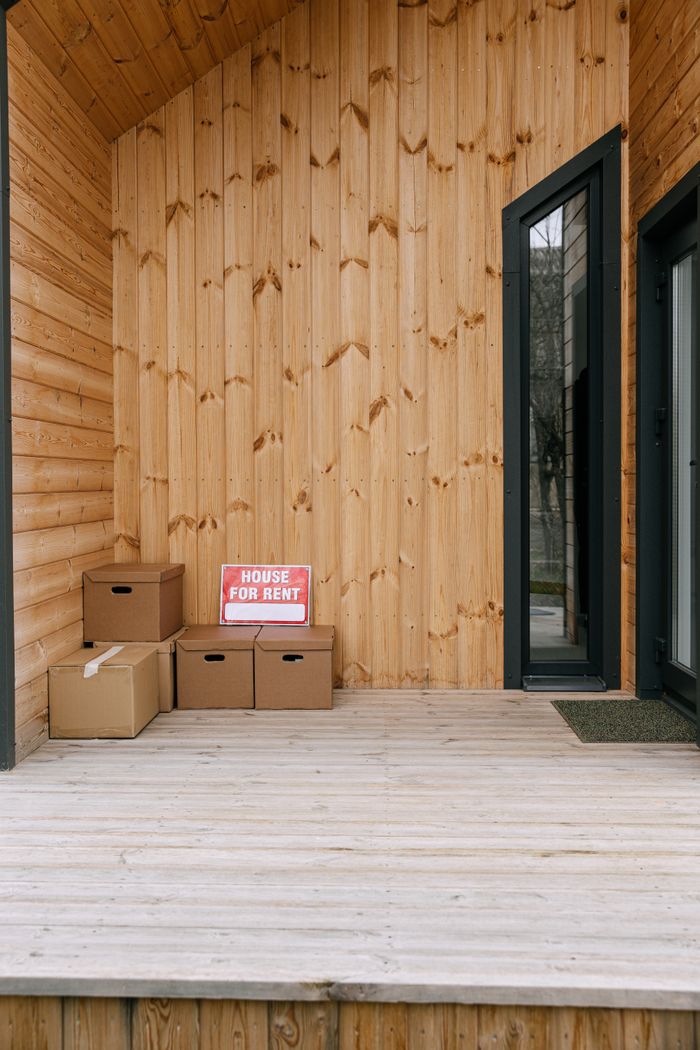 A wooden porch with boxes and 'House for Rent' sign, perfect for real estate listings.